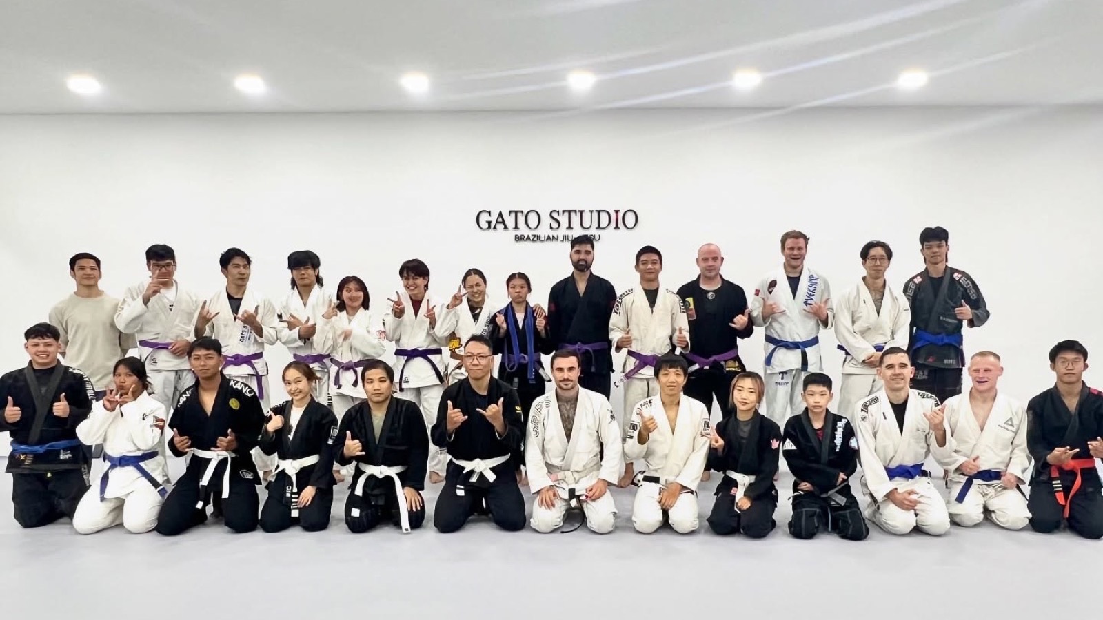 นักเรียนทั้งคลาสของ Gato Studio BJJ ถ่ายรูปรวมกันหน้าโลโก้ยิมที่เชียงใหม่